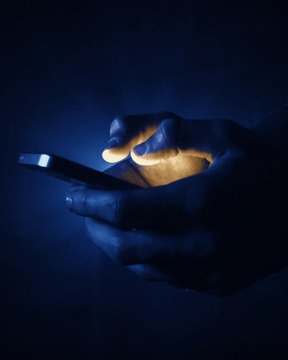 Hands holding a glowing phone in navy light